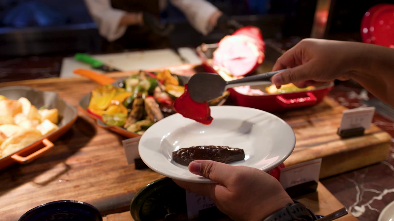 A person uses metal tongs to serve grilled zucchini and red bell peppers onto a plate