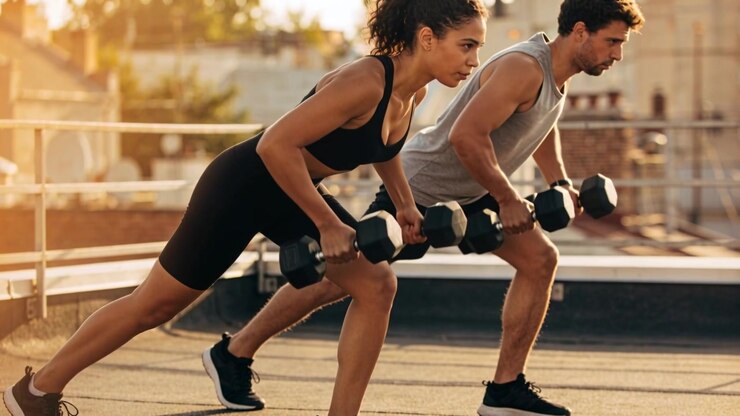 Holding low position, man and woman in sportswear doing rows with hex dumbbells rooftop training
