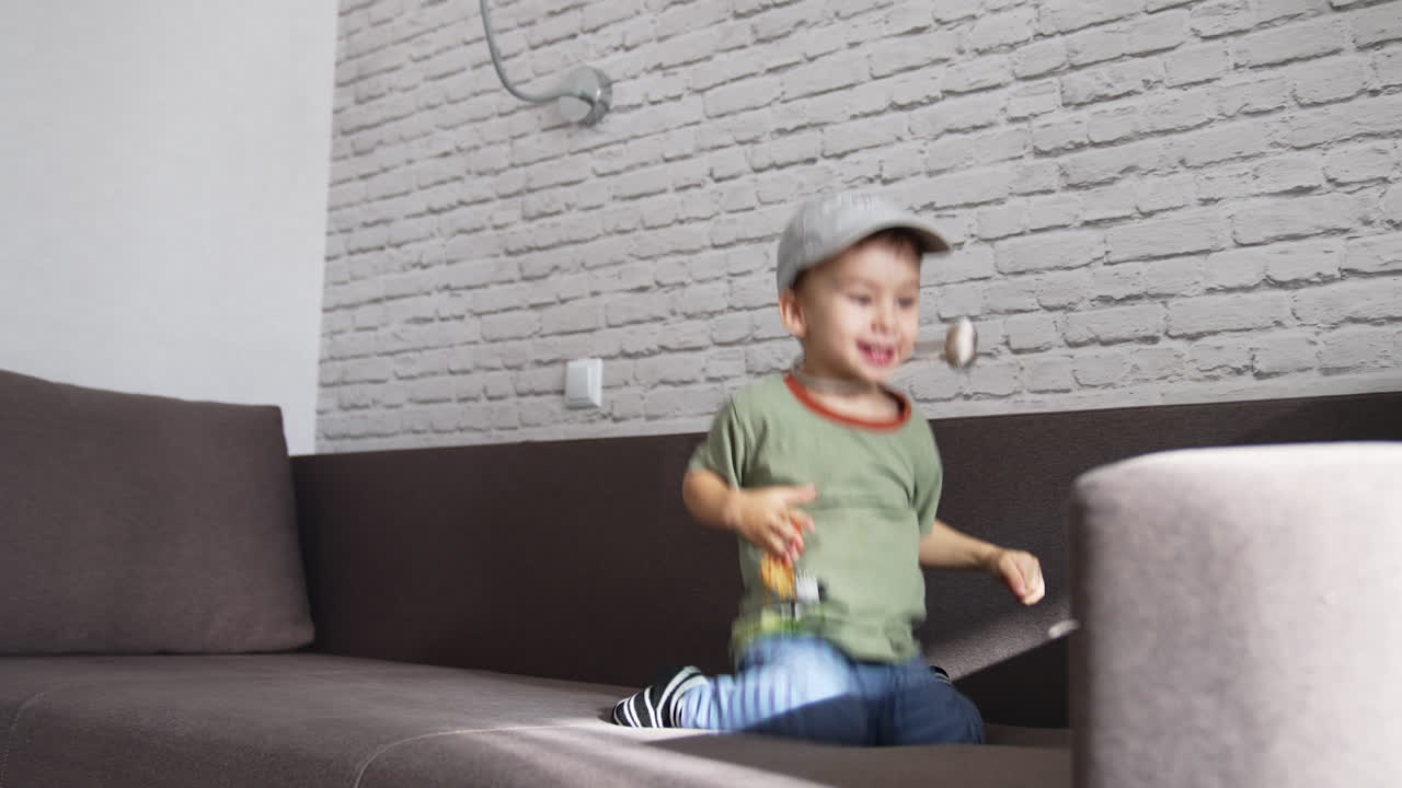 Happy energetic toddler boy jumping on the sofa. Funny kid having fun playing at home.