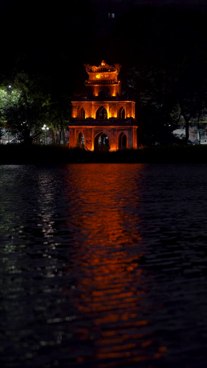Vertical shot of illuminated Turtle Tower on Hoan Kiem Lake with a reflection on the water - Hanoi, Vietnam