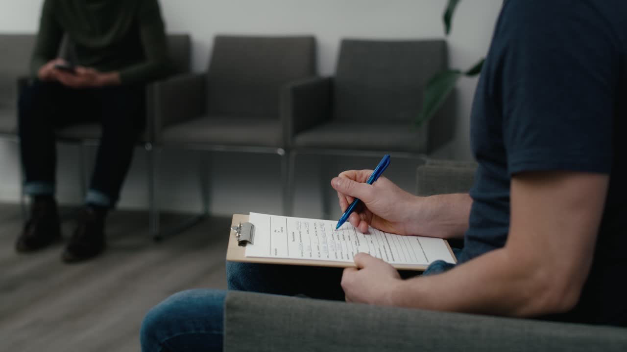 Ugenkendelig mand sidder i venteværelse og udfylder dokumenter.