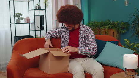 glücklicher junger käufer auspackt kartonbox, liefert paket, kauft online, kauft zu hause