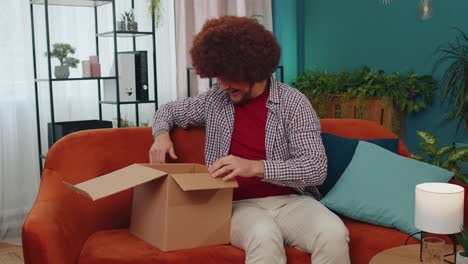 happy young man shopper unpacking cardboard box delivery parcel online shopping purchase at home