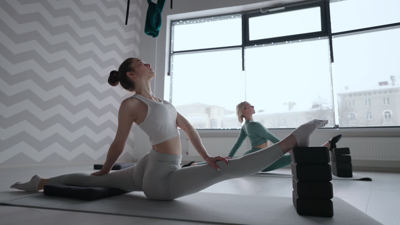 Due donne sullo sfondo della finestra fanno stretching in uno studio sportivo. Esercizi di stretching. Le donne praticano esercizi Pilates per la salute.