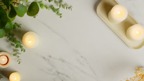 Overhead-View-Looking-Down-On-Still-Life-Of-Lit-Candles-With-Dried-Grasses-Green-Plant-And-Person-Picking-Up-Towels-As-Part-Of-Relaxing-Spa-Day-Decor