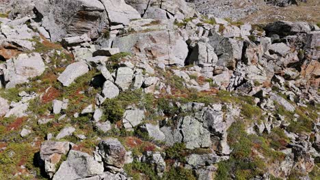 Ascending-aerial-view-of-two-hikers-on-rocky-peak-with-alpine-lake-on-sunny-summer-day