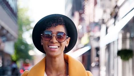 Millennial-schwarze-Frau-Trägt-Einen-Gelben-Erbsenmantel,-Eine-Sonnenbrille-Und-Einen-Homburg-Hut,-Steht-Auf-Einer-Stadtstraße-Und-Lächelt-In-Die-Kamera,-Aus-Nächster-Nähe