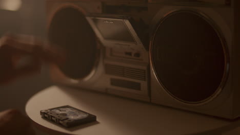 hand inserting compact cassette into boombox, then turning on music
