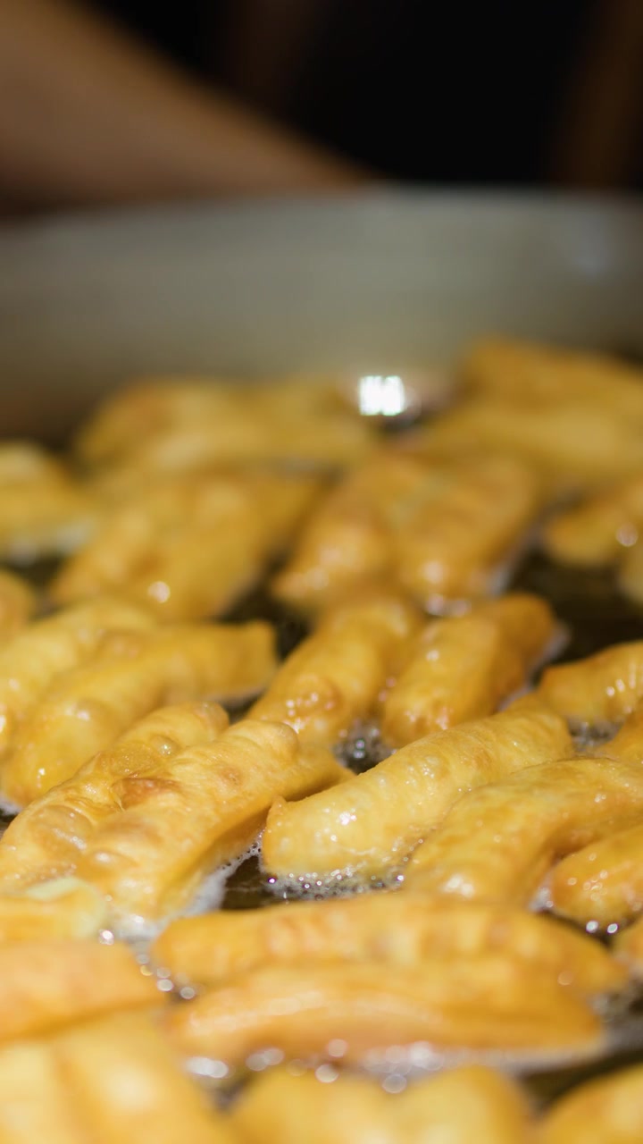 Friggere Youtiao (ciambelle cinesi) in olio bollente