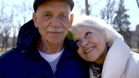 Camera-zooming-out-of-a-senior-couple-who-is-hugging-and-looking-at-camera-in-the-park-on-a-winter-day