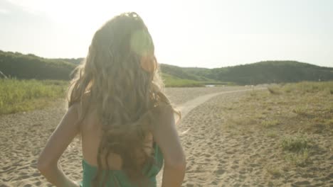 Jubilant-lady-with-blonde-hair-in-green-dress-runs-on-beach-path,-follow-cam