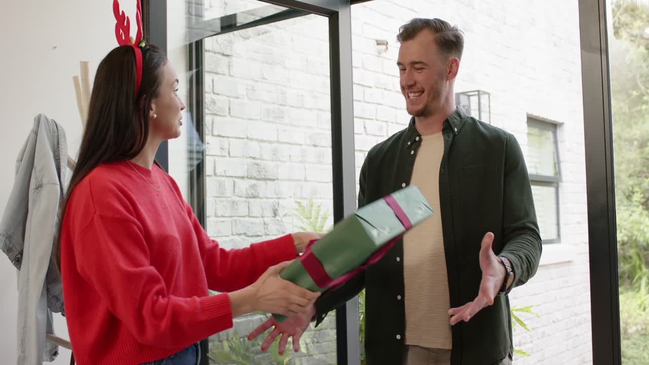 Amici che entrano nell'ingresso, abbracciandosi e tenendo del vino, poi offrendo un regalo incartato e abbracciandosi