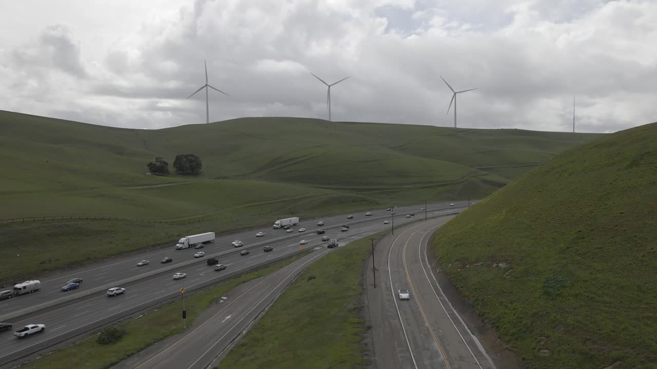 Under a cloud-draped sky, this drone footage uncovers Highway 580's tranquil journey through the windmill-studded, verdant hills of Altamont Pass, lightly peppered with sparse yet constant traffic