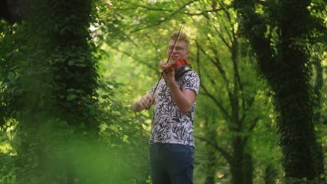 Enthusiastic-young-caucasian-fiddler-plays-the-violin-in-lush-green-forest