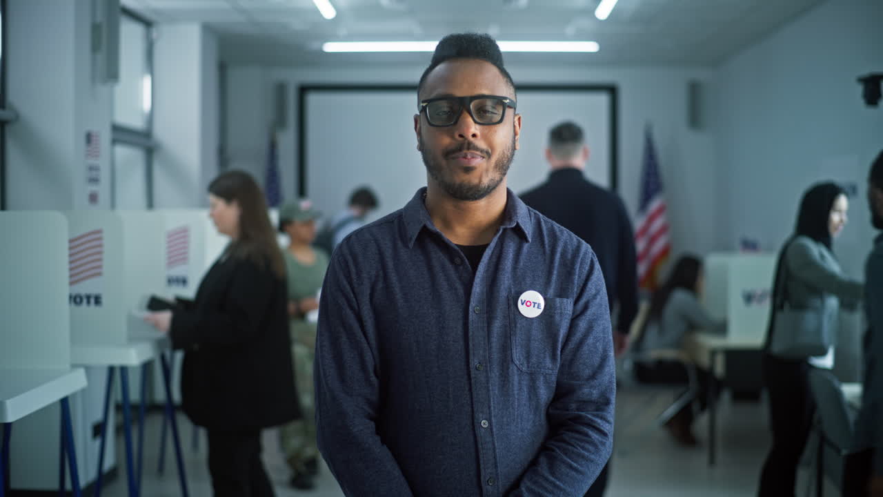 Portrait of African American Man Usa Elections Voter Portrait of African American Man United States of America Elections Voter Man with Badge Stands in Modern Polling Station Poses Looks at Camera Background with Voting Booths Election Day in Usa