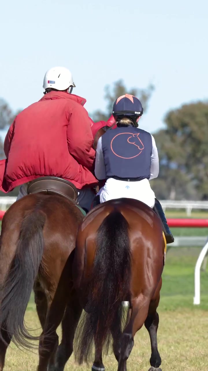 Vista trasera de dos jinetes montando caballos marrones en un hipódromo soleado en Australia