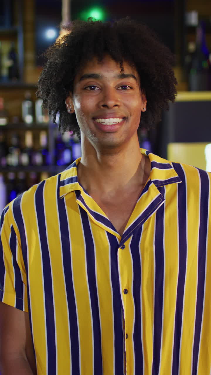Vertical video of happy african american man smiling to camera at a bar