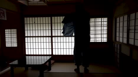 silhouette of male waking and putting on kimono shirt inside dim lit ryokan with backlit shoji doors