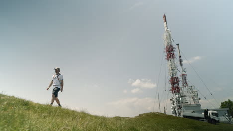 excursionista con gorra y mochila alejándose de una torre de radio en nanos de montaña en un día de verano