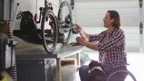 hombre caucásico con discapacidad en silla de ruedas reparando bicicleta en el garaje