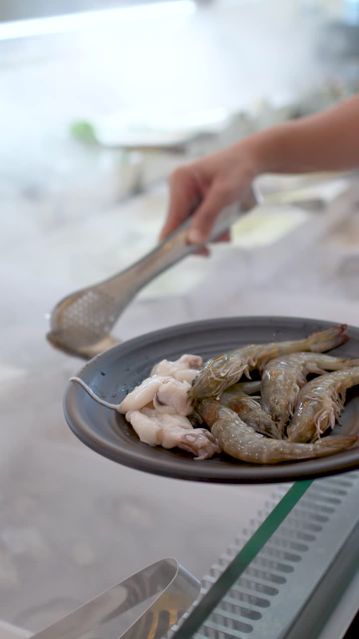 Close-up of a hand using metal tongs to select fresh seafood from a buffet display