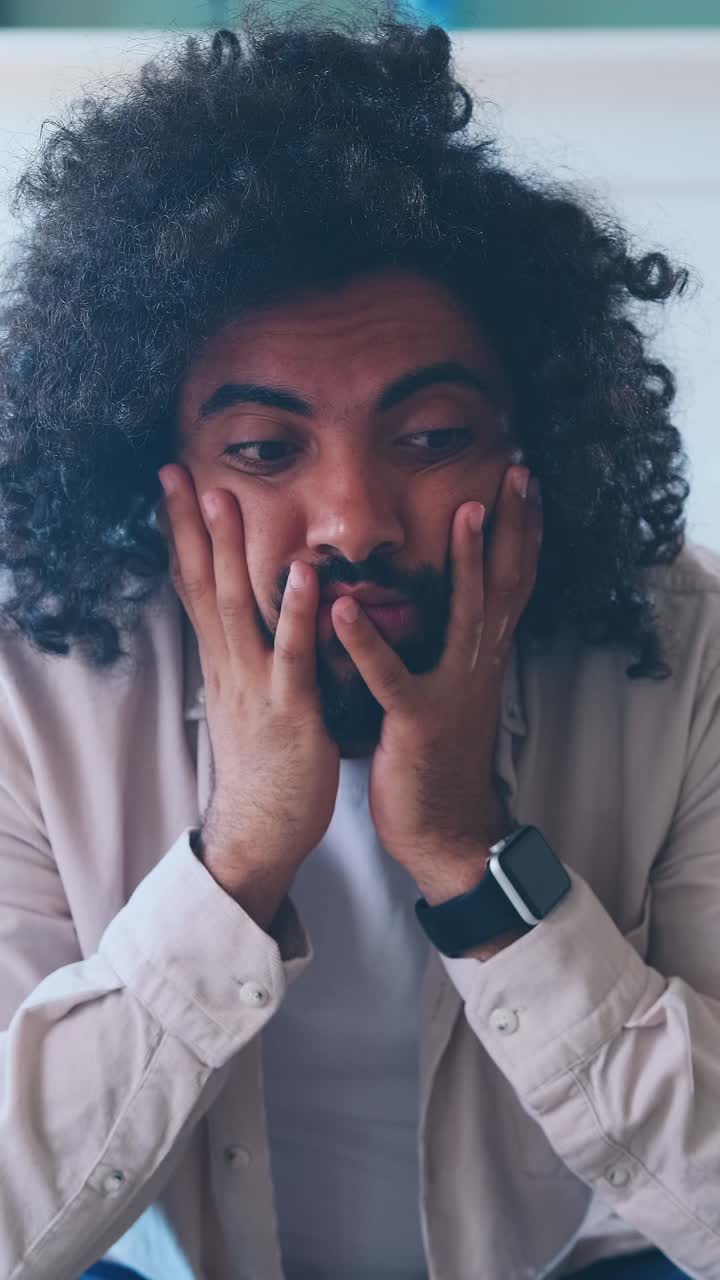 Young tired worried arabian man feels excited sits on couch in apartment