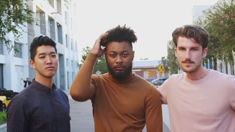 three young adult male friends standing in a city street looking to camera, front view, close up