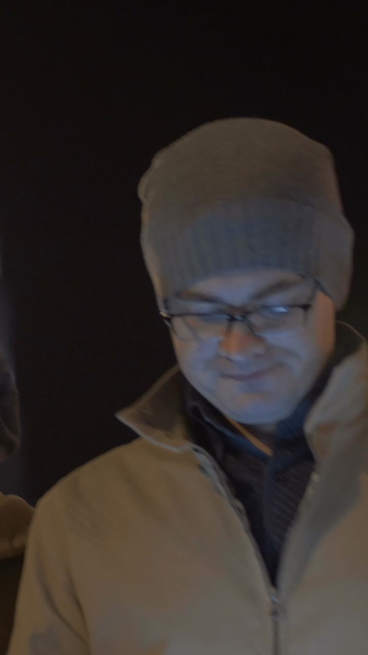 Man with Glasses and Hat Looking at Tablet at Night