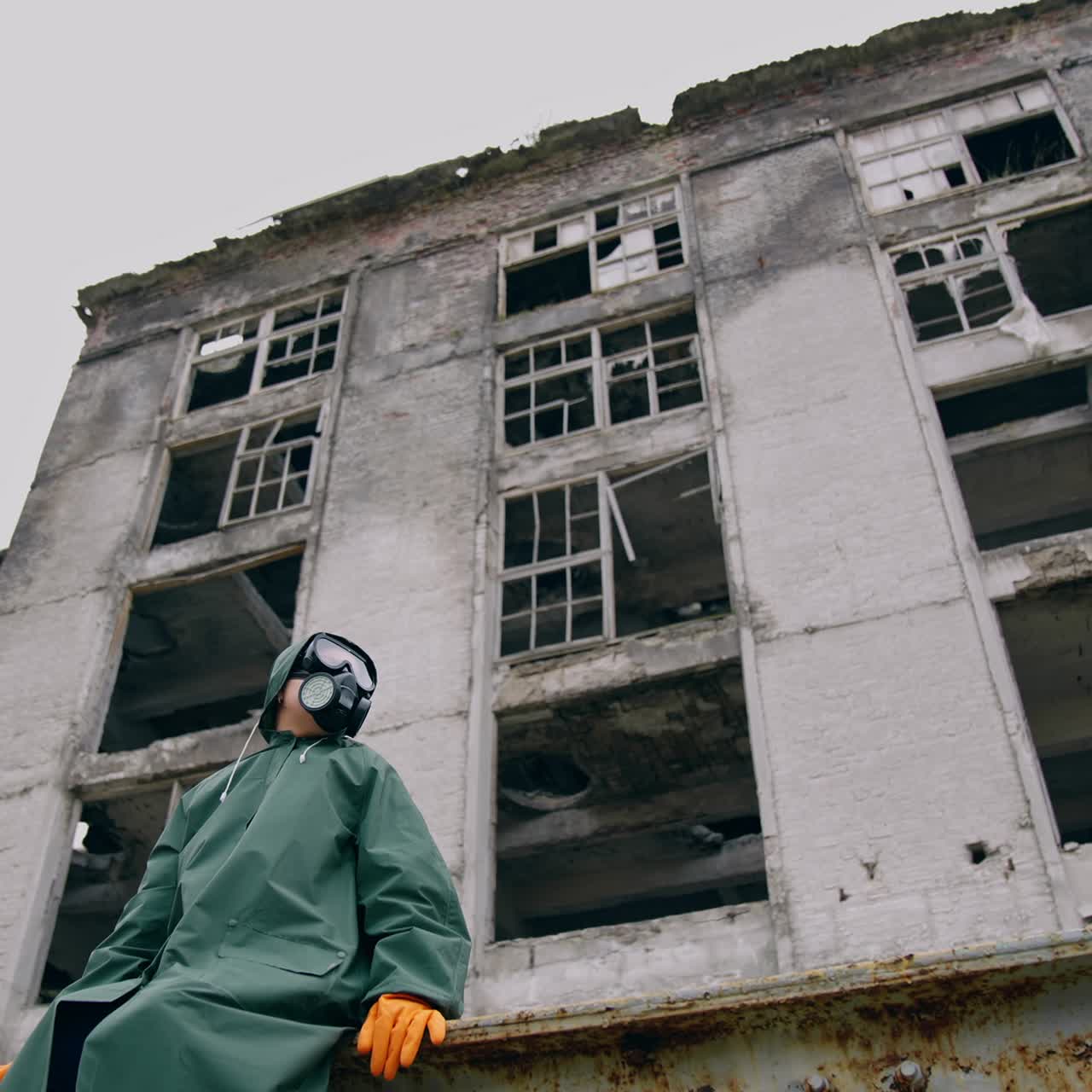 Woman in respirator and protective coat. Survivor on the background of ruined building without windows, Chemical pollution in the city. View from below