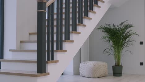 a serene home entry with a modern staircase, wooden steps, plush pouf, and a tall indoor plant enhancing the natural decor.