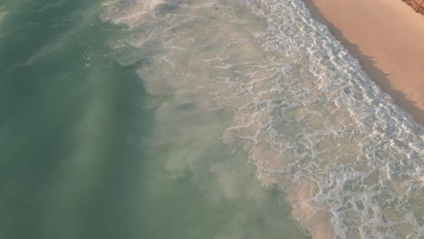 Aerial-view-of-gentle-waves-lapping-a-sandy-beach