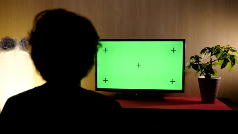 view from the back woman sitting in the living room and watching tv with green screen.