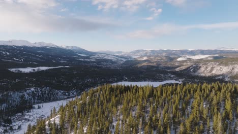 drone flying past top of mountain to reveal valley with rocky mountains at distance in colorado, usa.