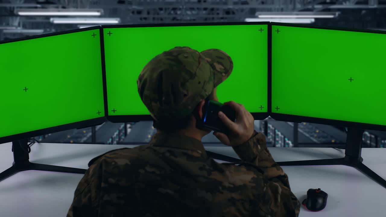 vista trasera de militares asiáticos hablando en teléfono móvil mientras trabajan con monitores de computadoras múltiples en el centro de datos