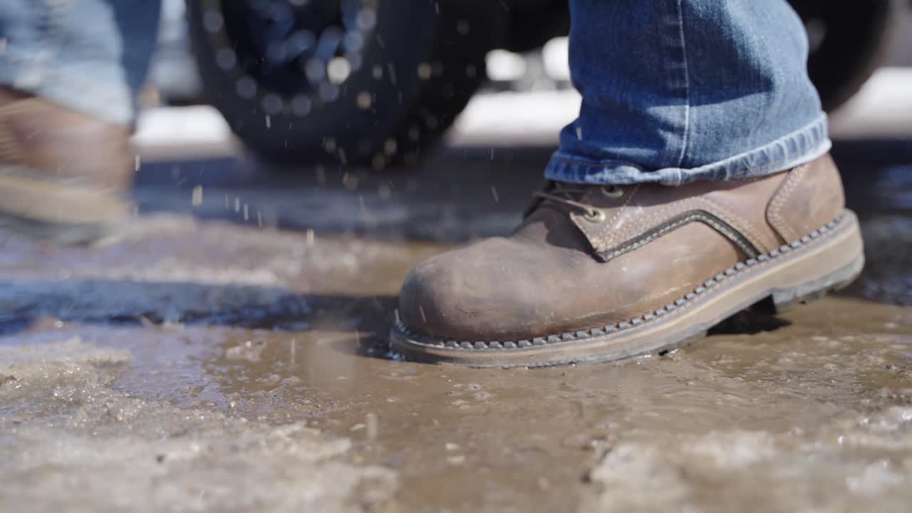 Close up, man's rugged work boots splashing puddle while getting truck