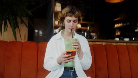 una mujer joven disfrutando de un batido y usando su teléfono en un café