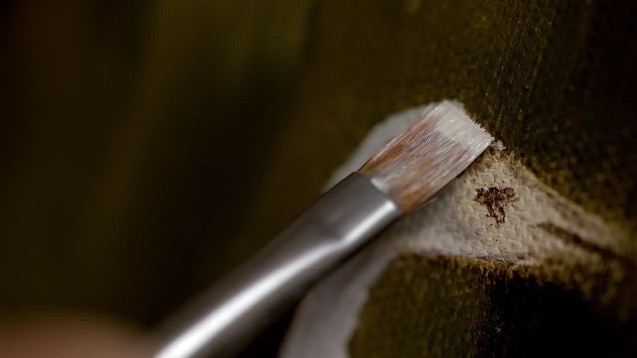 primer plano detallado de un pincel de punta fina y ancha extendiendo pintura blanca en el lienzo