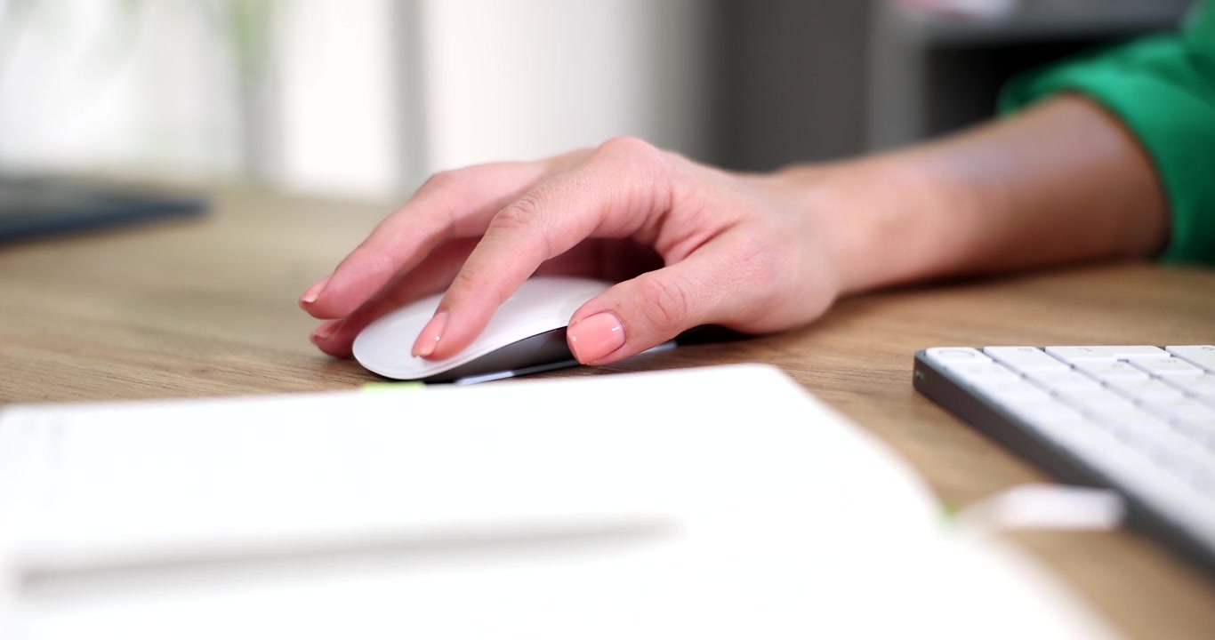 Donna usa un mouse bianco per computer su una scrivania di legno con tastiera