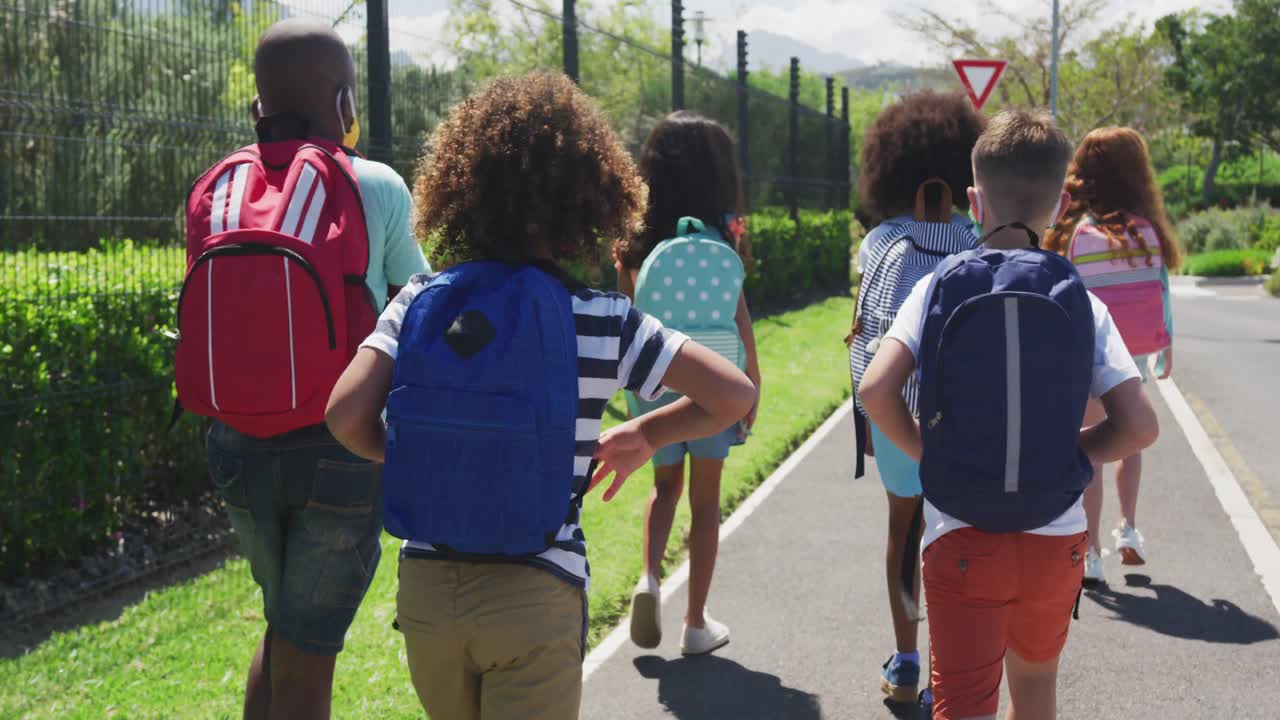Rear view of group of kids wearing face masks walking on the road