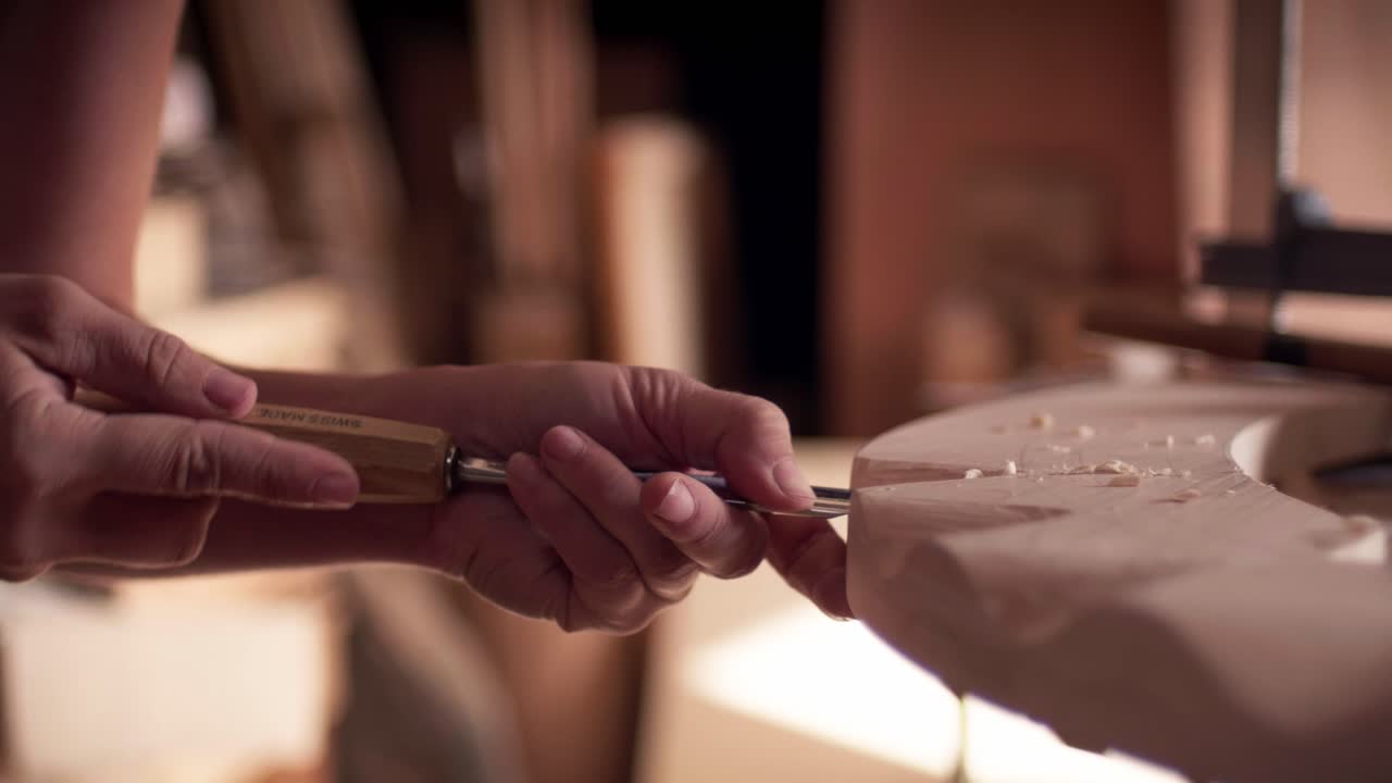 Professional female woodworker carefully using a hand chisel to shape a piece of wood in a workshop. Slow motion