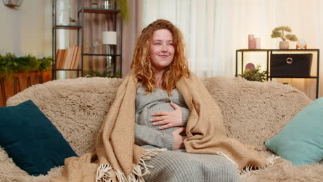 Pregnant young woman wrapped in warm blanket at home gently hugging belly cozy and comforting moment