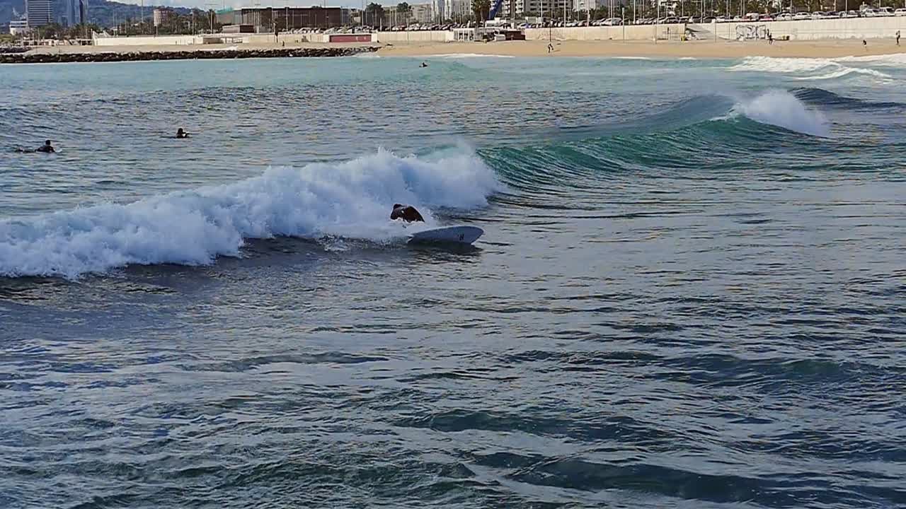 Slow motion (120fps): male surfer surfing the wave among other surfers in Barcelona, Spain