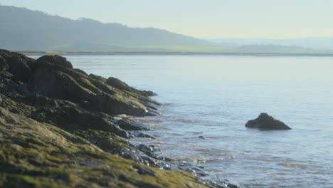 sea washing against rocks on shoreline with misty hills in distance