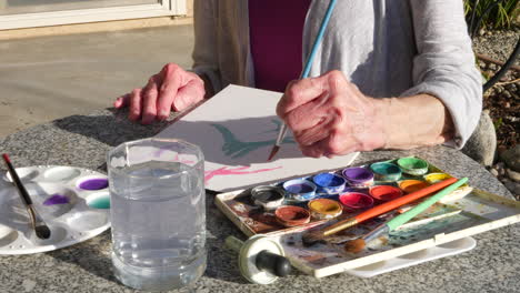 an elderly woman artist painting with watercolors to relieve stress and relax in an outdoor art studio