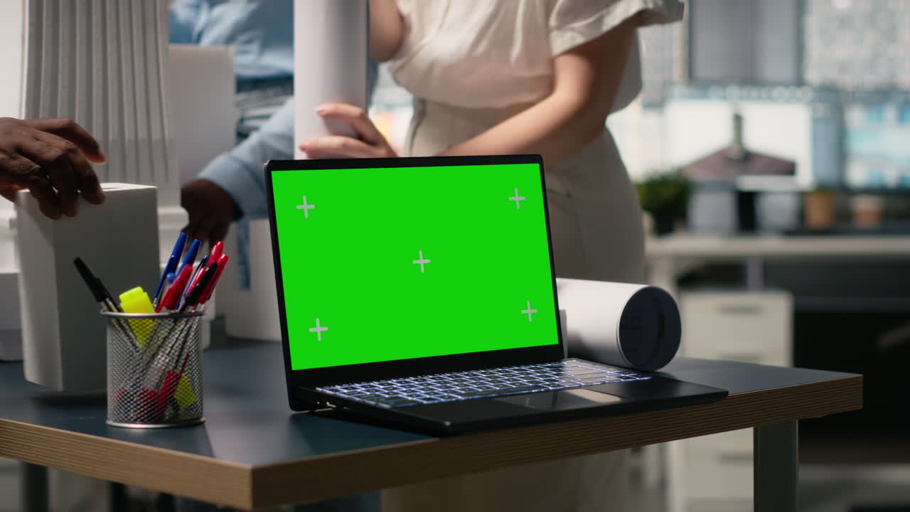 Laptop with green screen on a desk with architects in the background