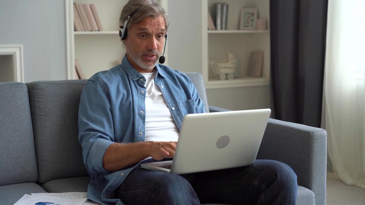 Moden mand, der arbejder på bærbar computer med headset i sofaen