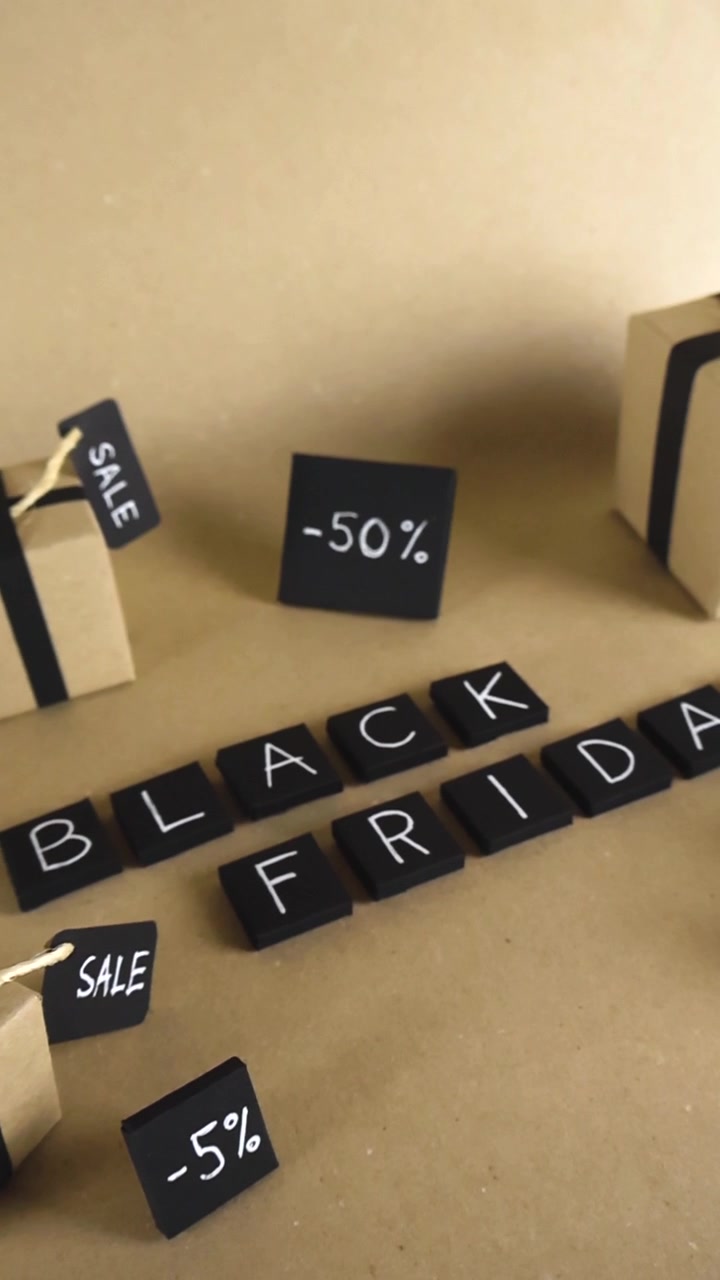 Płynne ujęcie ślizgowe nad ręcznie wykonaną sceną promocyjną z napisem Black Friday, małymi pudełkami prezentowymi z metkami wyprzedażowymi i różnymi znakami procentowych zniżek na tle papieru pakowego.