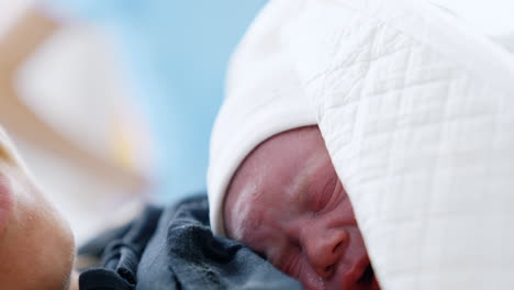 little red crying newborn lying on his mom's chest. just born baby covered in blankets. close up portrait.