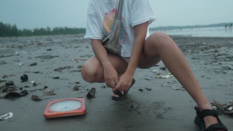 girl next to a wall clock that sank on the black sand beach full of trash