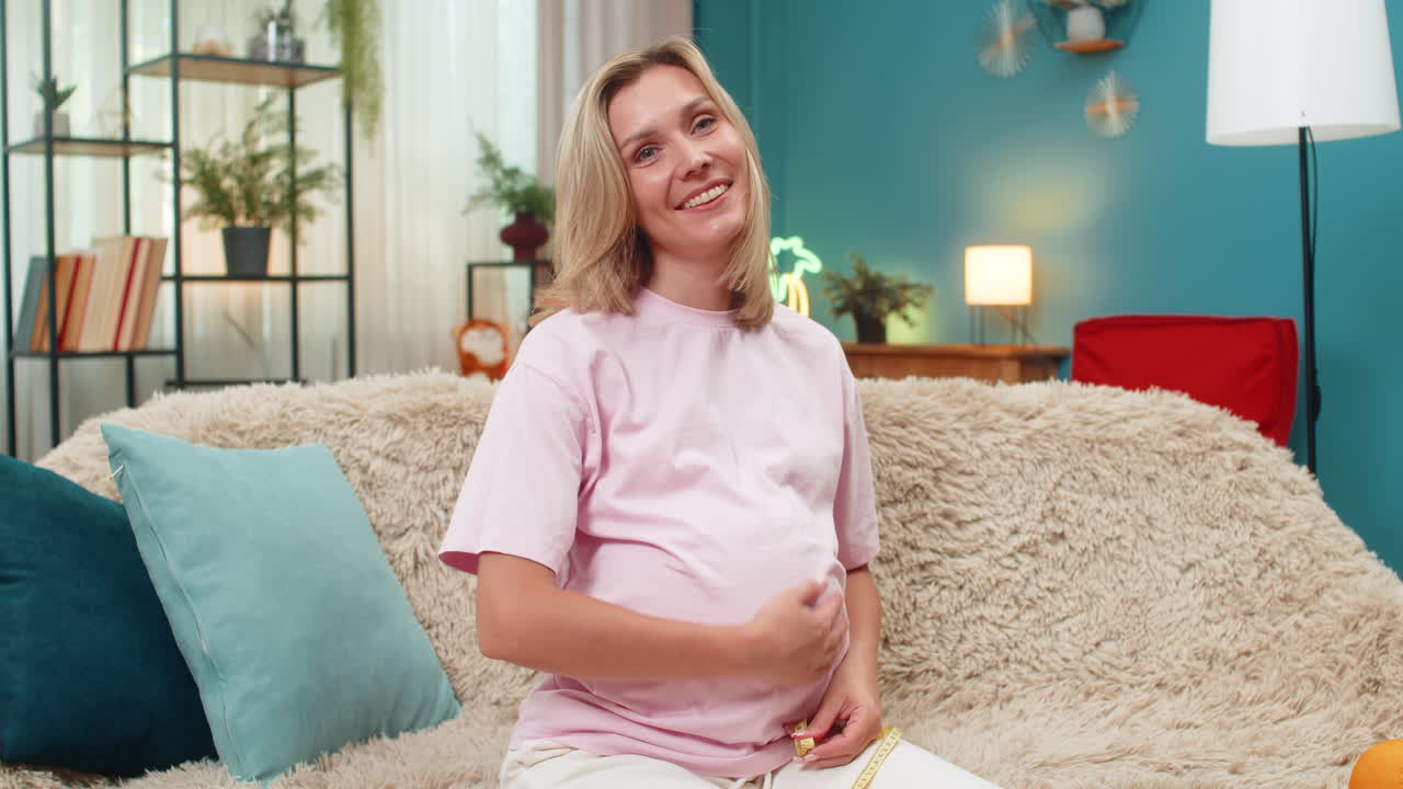 Pregnant woman measuring belly with tape smiling satisfied with progress expecting baby birth soon